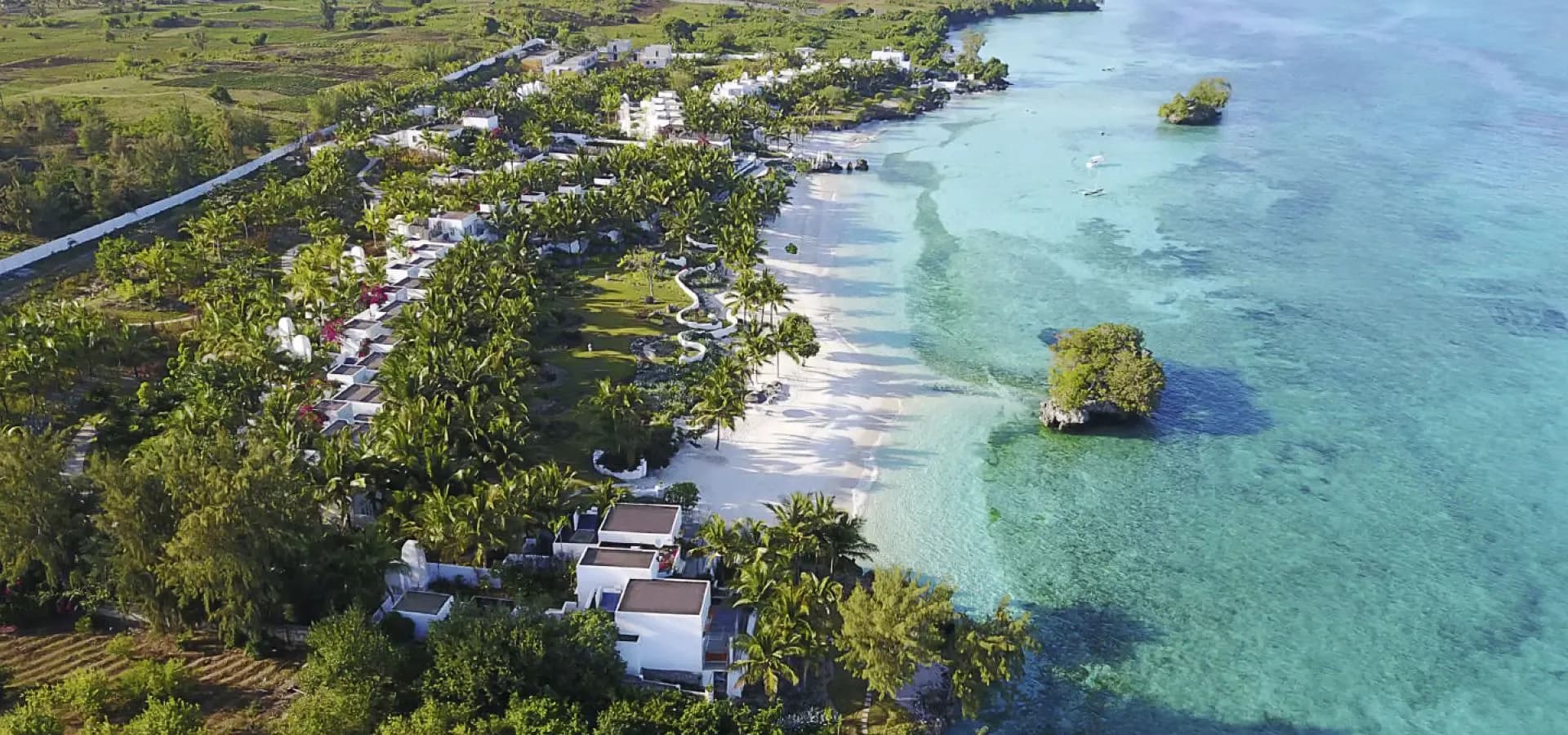 Aerial view of a resort with thatched roofs beside a turquoise sea