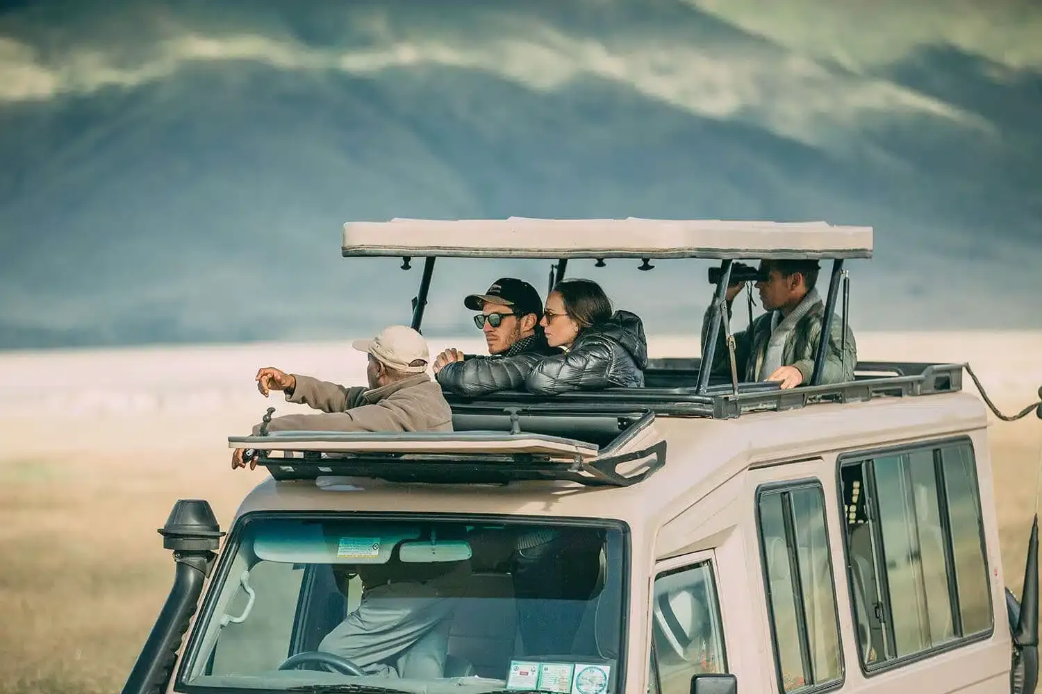 Guests in an open-roof safari vehicle looking out across open grassland with hills in the distance