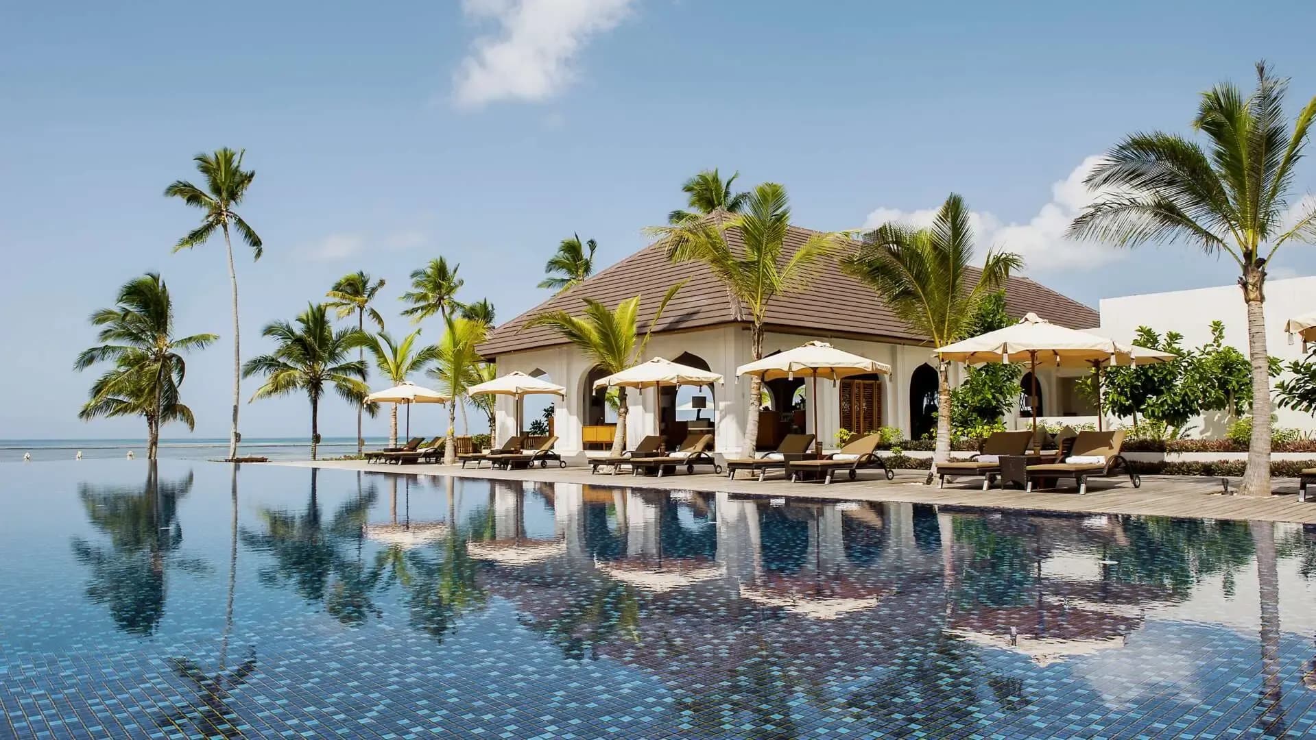 The infinity pool and palm-fringed pavilions of The Residence Zanzibar, with umbrellas along the water
