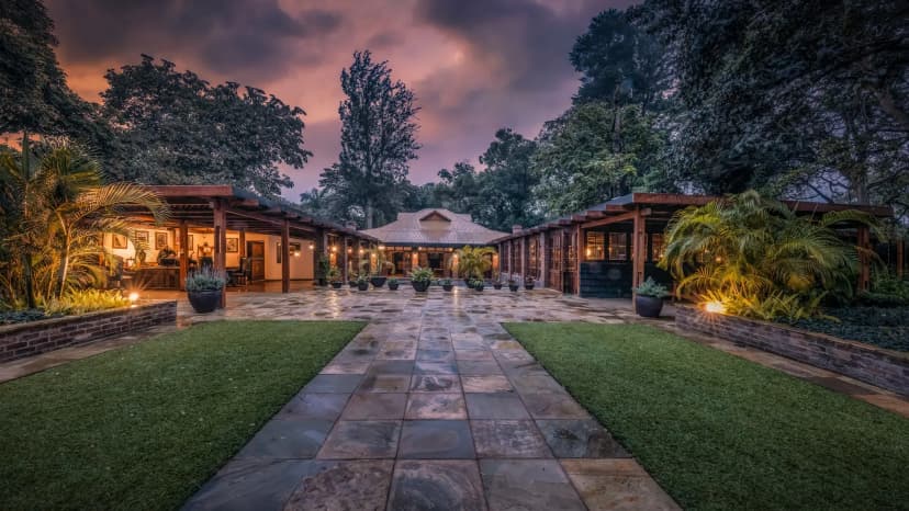 The stone-flagged path and lit pavilions of Arusha Coffee Lodge's gardens at dusk