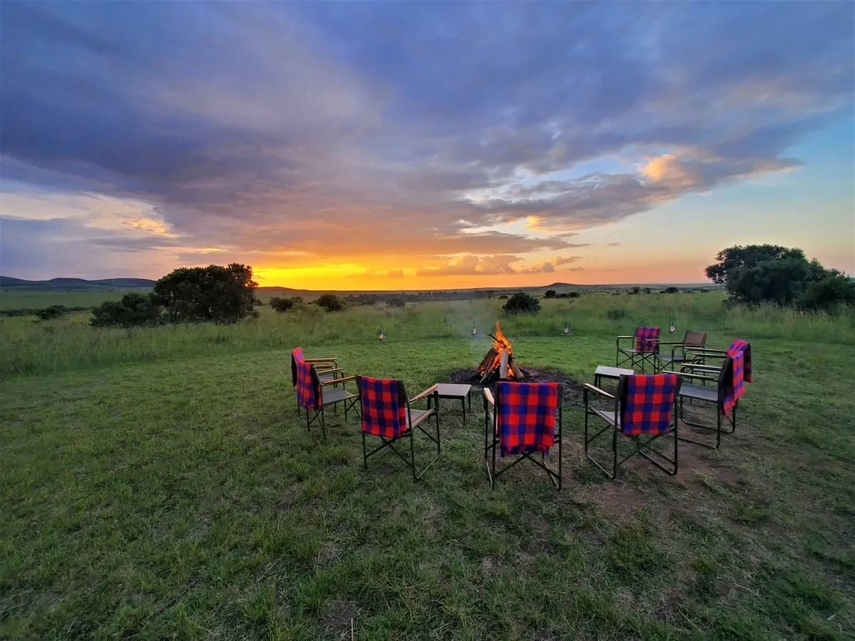 Folding camp chairs around a fire pit on open grassland under a sunset sky